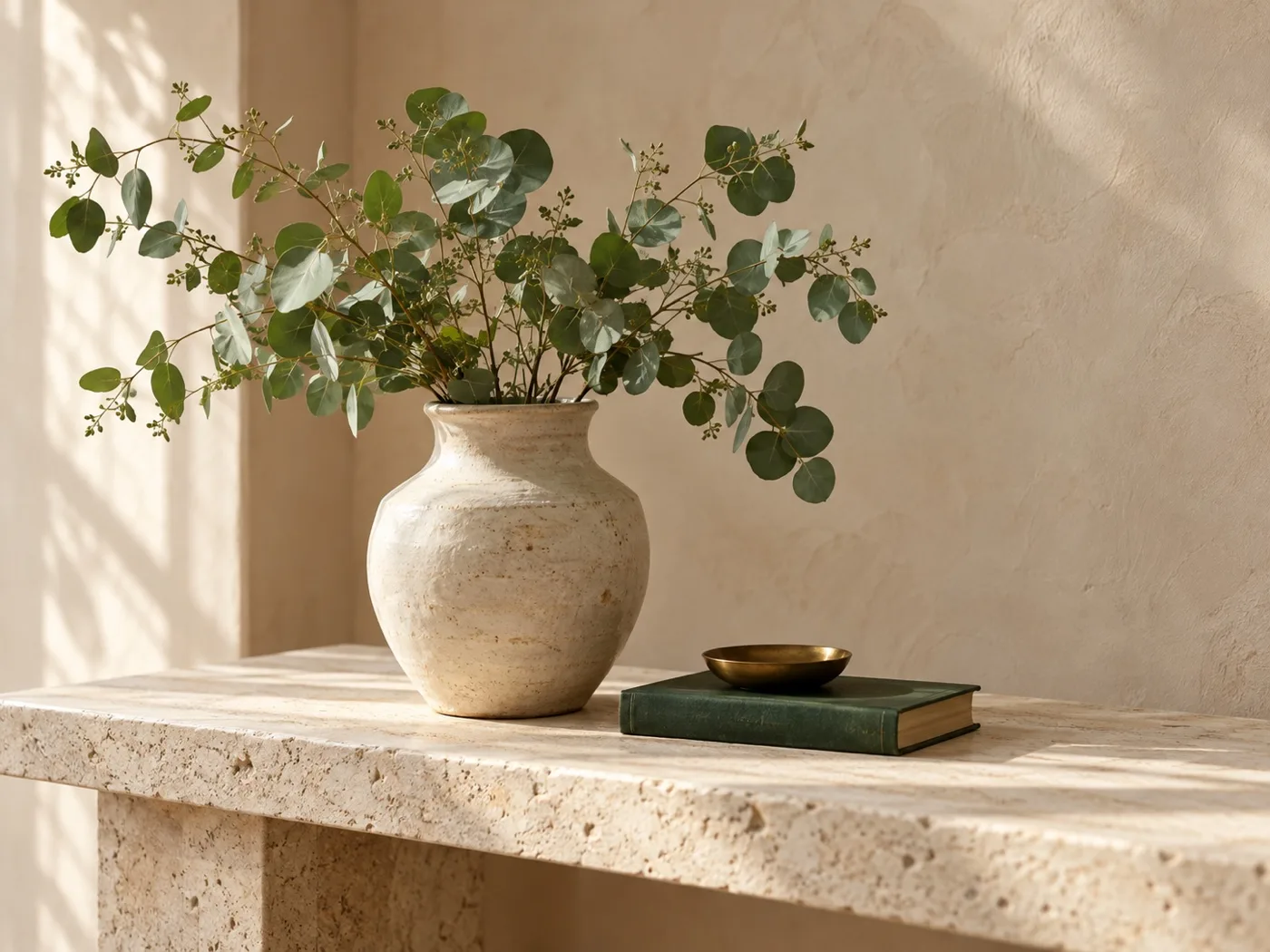 Before: ceramic vase with eucalyptus, a dark-green book, and a brass dish on a console